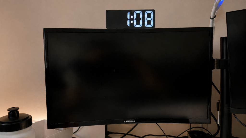 Digital clock mounted above a computer monitor showing the time.